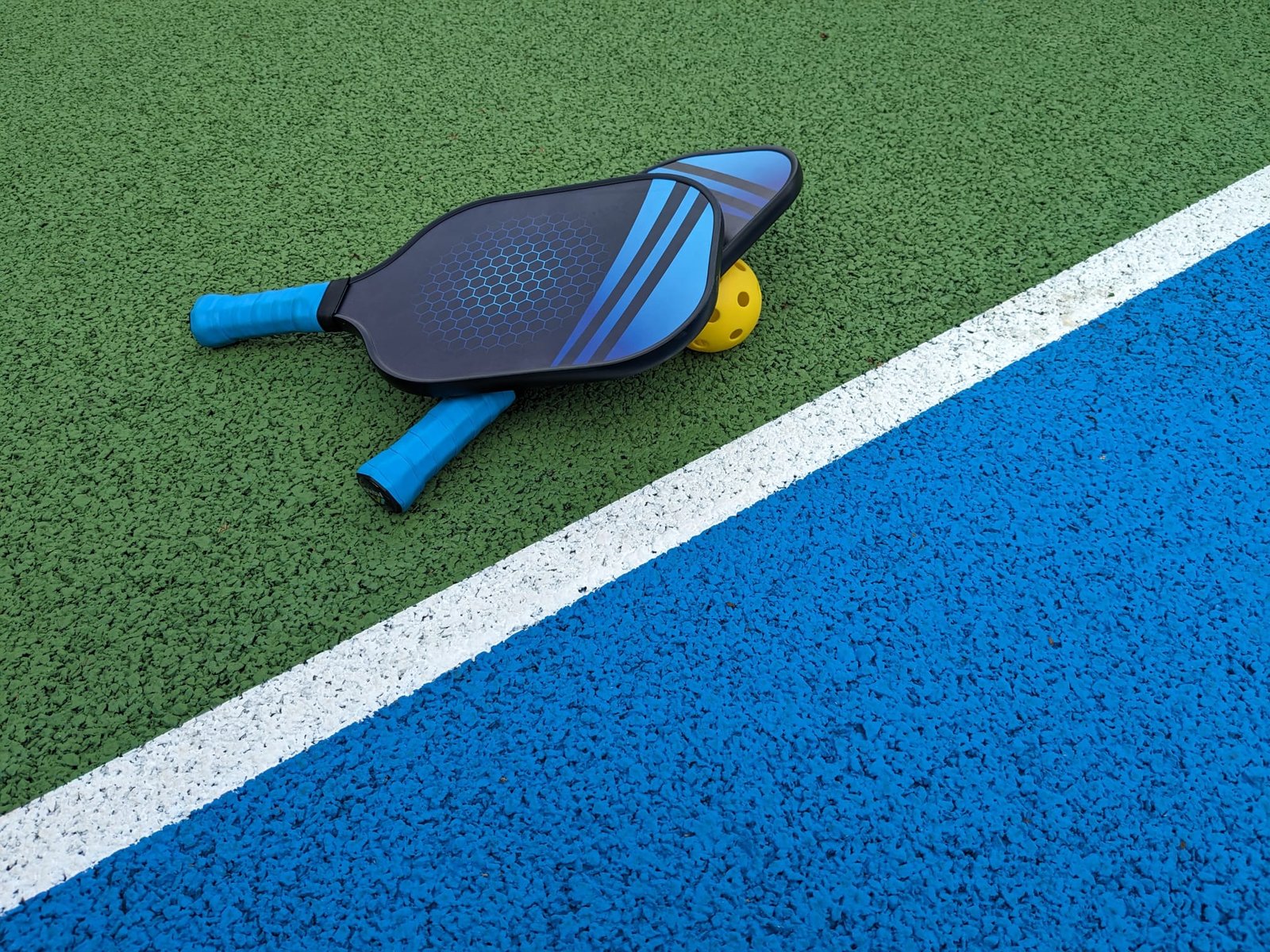 An artistic shot of two paddles balancing on a ball on a pickleball court in North London